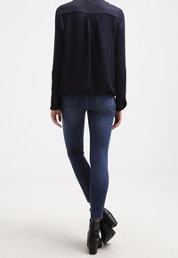 Marinblå långärmad skjorta med yoke-design och knappmanschetter, tillsammans med mörkblå slim fit-jeans och svarta ankelstövlar.