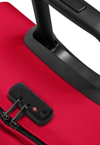 Red suitcase with textured fabric, black hardware, and a combination lock featuring silver zippers and a retractable handle.