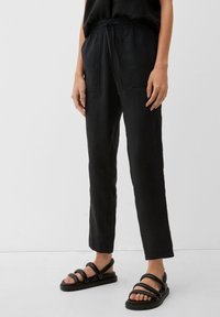 Svarta linnebyxor med en avslappnad passform, med elastisk midja och två framfickor, i kombination med svarta sandaletter med remmar.