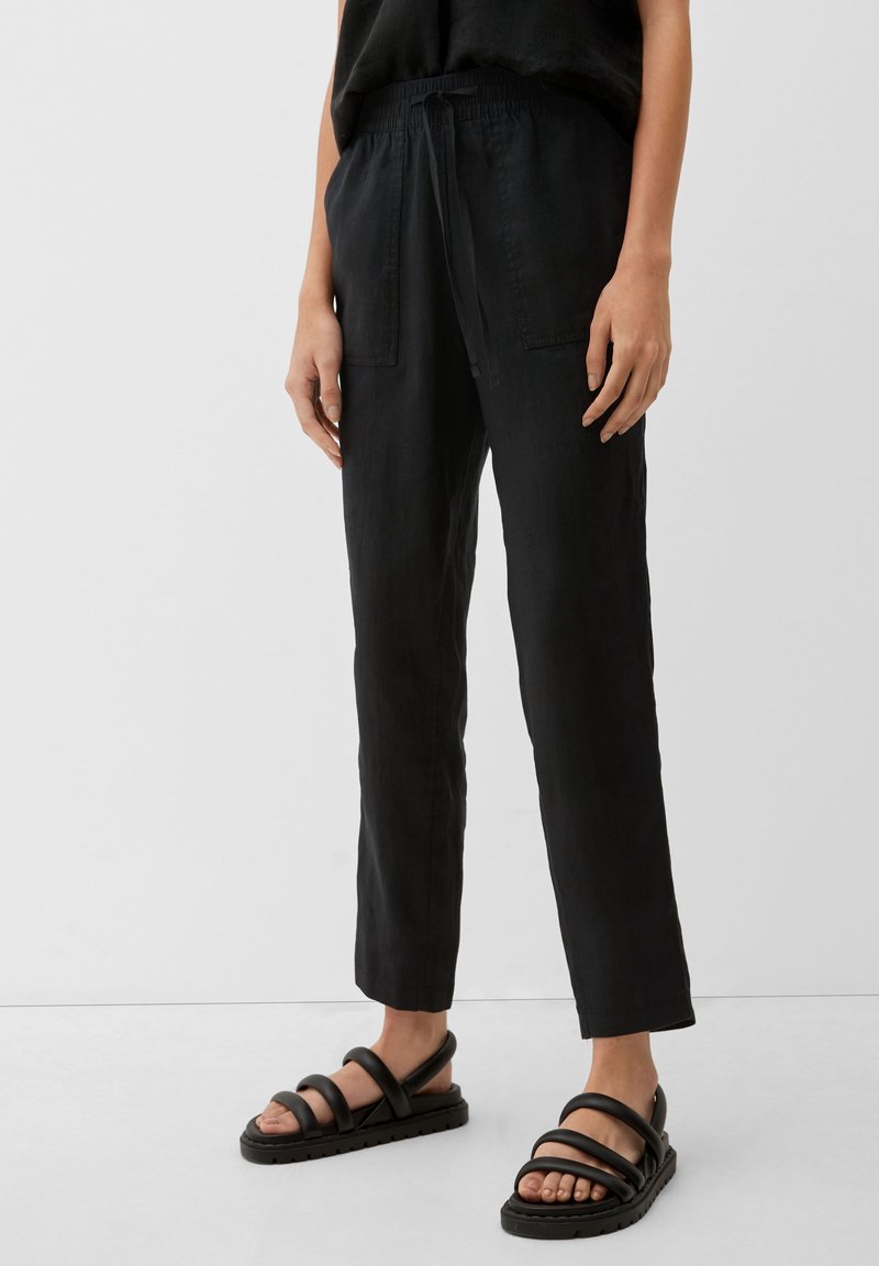 Svarta linnebyxor med en avslappnad passform, med elastisk midja och två framfickor, i kombination med svarta sandaletter med remmar.