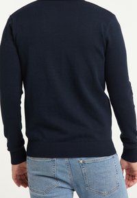 Mörkblå stickad tröja med långa ärmar och ribbade manschetter. Slät textur och figursydd design, kombinerad med ljusblå denimjeans.