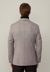 Blazer gris ajusté avec une texture lisse, fente arrière simple et coudières. Le col a un accent contrastant en bleu marine.