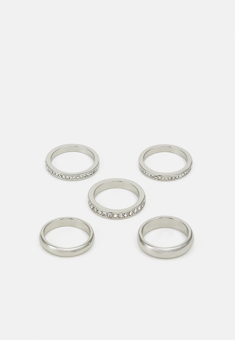 Sett med fem sølvringer i forskjellige design, inkludert én med en rad av klare steiner. Glatt og reflekterende metallfinish.