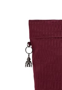 Burgundy tote bag made of textured fabric, featuring a decorative keychain with a monkey figure and a top opening with stitching details.