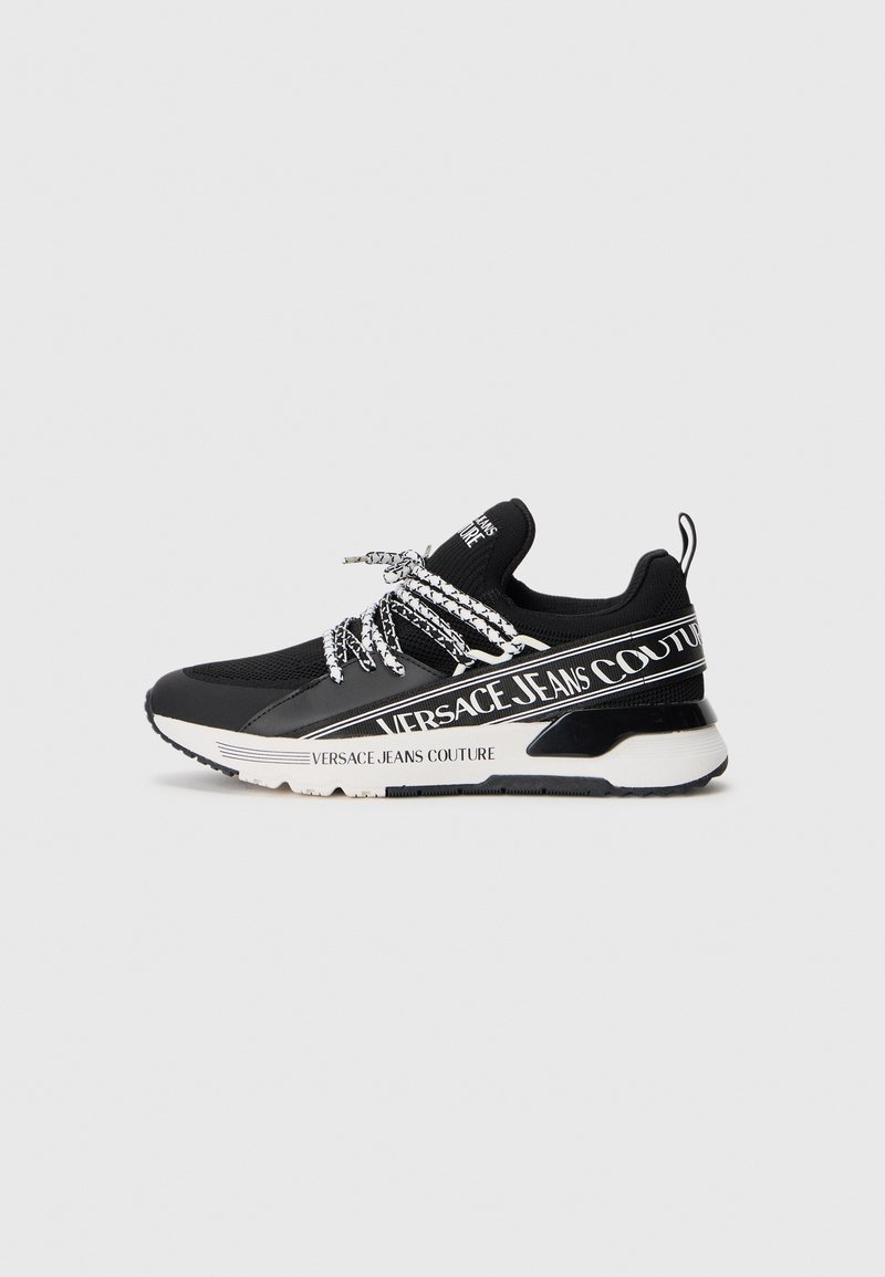 Sneakers atléticos pretos com um upper texturizado, marcação branca e atacadores pretos em contraste. Apresentam uma entressola branca espessa e sola de borracha.