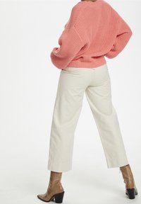 Maglione rosa a maglia con spalle scese, abbinato a pantaloni crema a gamba larga e stivaletti marroni con tacco. Tessuto texturizzato e vestibilità rilassata.
