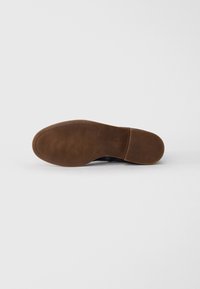 Semelle en caoutchouc marron avec une texture antidérapante, légèrement courbée. Conçue pour le confort, avec une partie supérieure lisse et foncée.