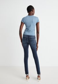 T-shirt fitted blu chiaro con maniche corte, abbinato a jeans skinny blu scuro con tasche posteriori e dettagli di cucitura sottili.