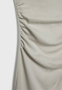 Tissu beige clair avec un détail froncé vertical rassemblé le long du bord gauche, créant des plis doux et une texture.