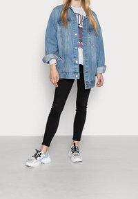 Světle modrá džínová bunda s klopovými kapsami, oversize střih; šedé tričko s grafikou pod ní; černé skinny džíny; masivní bílé a modré tenisky.