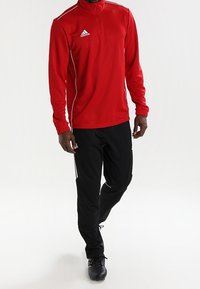 Rode zip-up sportjack met witte piping, gecombineerd met zwarte broek met witte zijstrepen. Beide gemaakt van lichtgewicht stof.