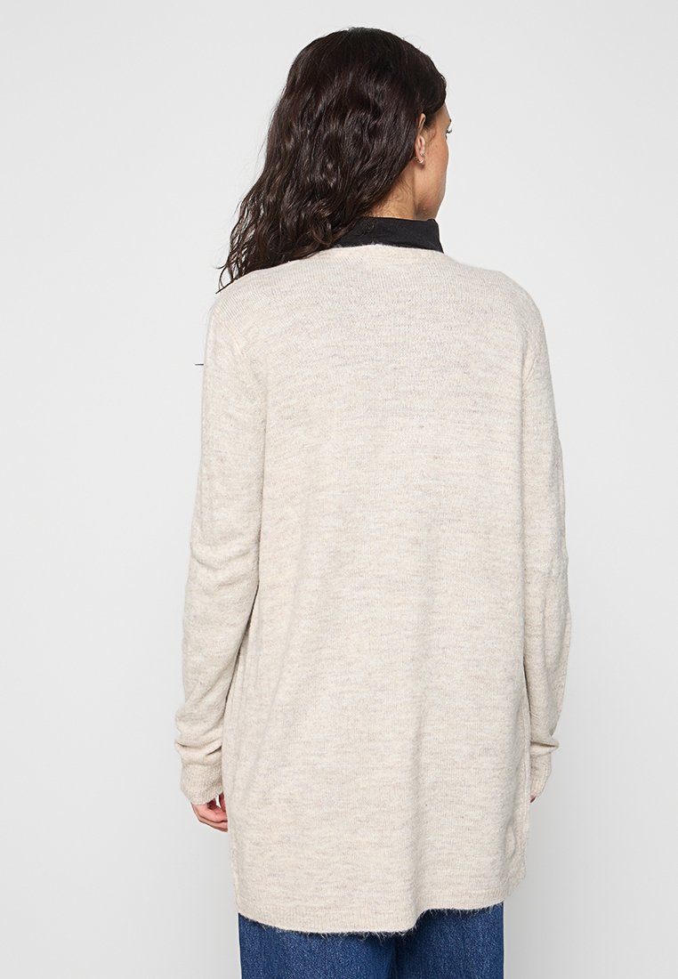Lange beige cardigan van zacht gebreid materiaal, met een afgeronde zoom en verlaagde schouders. Geen zichtbare patronen of hardwaredetails.