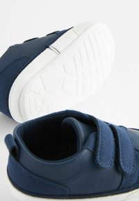 Baskets bleu marine en matériaux daim et cuir, avec une semelle en caoutchouc blanc, des sangles Velcro et une surface texturée sur la semelle.