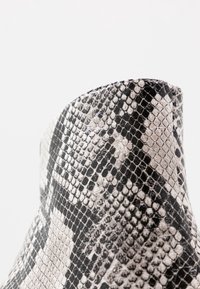 Black and cream snake-print ankle boot with a textured surface. Features a pointed toe and a sleek silhouette. Smooth finish.