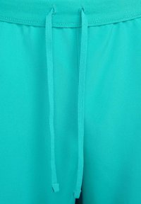 Calções turquesa com textura suave, com cintura ajustável por cordão e costuras detalhadas. O tecido parece leve e respirável.