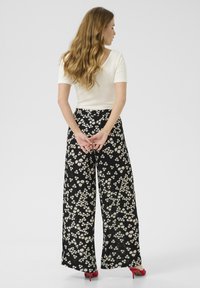 Haut blanc ajusté à manches courtes associé à un pantalon noir à jambes larges avec un imprimé floral. Des talons hauts rouges complètent la tenue.