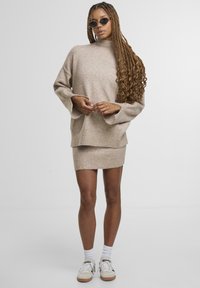 Beige kötött pulóver magas nyakú, harangujjú, amelyhez egy illő mini szoknya van párosítva. Fehér zoknikkal és sportcipővel viselve.