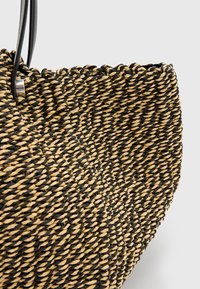 Borsa a tracolla intrecciata con fibre nere e beige, dalla forma leggermente arrotondata e dalla superficie texture. Manici neri attaccati.