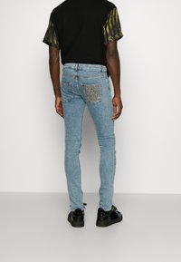 Jeans ajustados azul claro con un diseño texturizado en los bolsillos traseros. Llevados con una camiseta negra que presenta mangas cortas con un estampado verde.