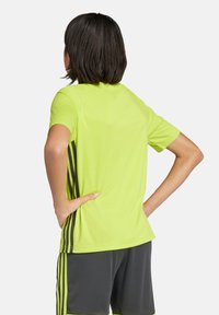 Camisa atlética verde neón de manga corta, con rayas laterales negras y un corte relajado. El diseño es ligero y suave.