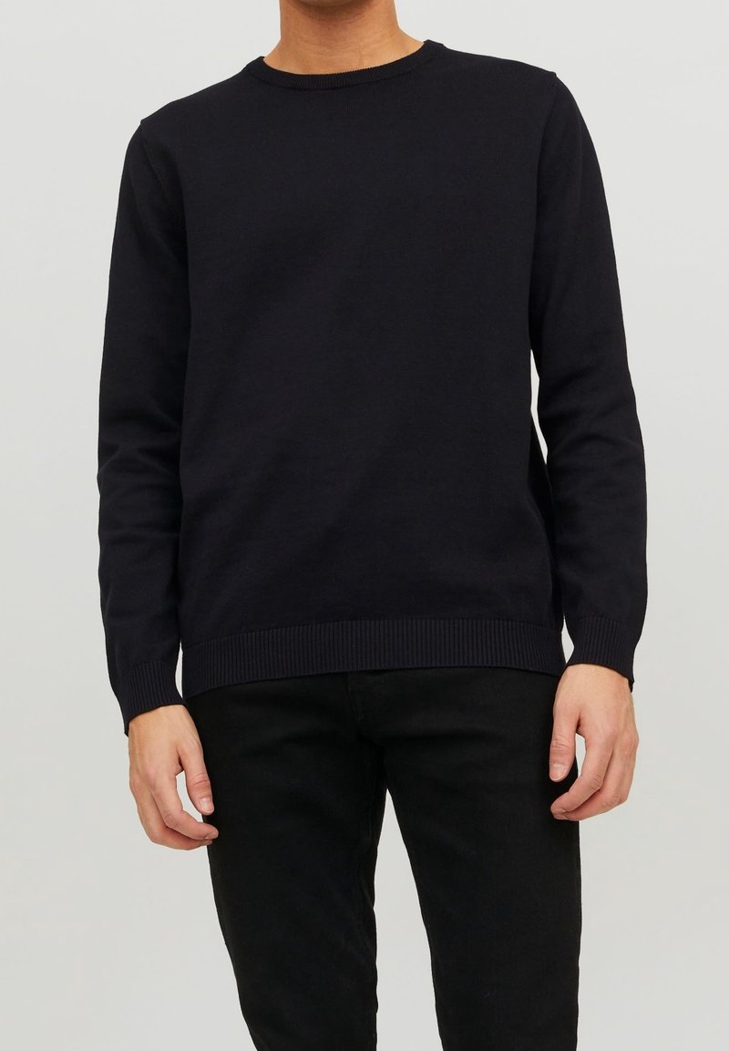 Pull en maille bleu marine avec un col rond, des poignets et un ourlet côtelés, porté sur un pantalon noir. Texture douce, coupe décontractée et manches longues.