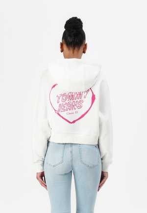 Haut à capuche blanc raccourci avec un graphique de cœur rose portant l'inscription "TOMMY JEANS Depuis 85" au dos. Assorti à un jean ajusté bleu clair.