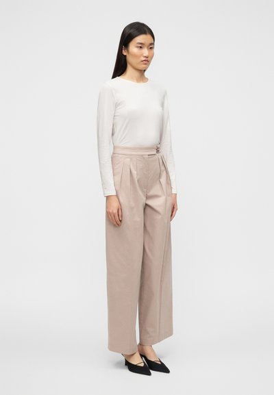 Μπεζ παντελόνι ψηλόμεσο με πιέτες, σε συνδυασμό με εφαρμοστή λευκή μπλούζα μακρυμάνικη. Παπούτσια με μαύρα μυτερά τακούνια. Απλός σχεδιασμός.