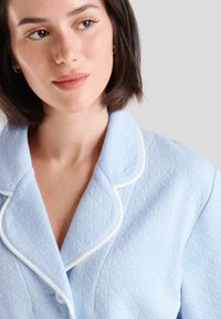 Camisón azul claro acolchado con un patrón de diamantes, que presenta un cuello blanco con ribete y botones, mostrando una textura de tejido suave.