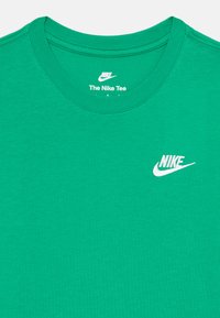 Zelena bombažna majica s krožnim izrezom, ki na levem prsnem delu vsebuje bel izvezen logotip Nike. Gladka tekstura, preprost dizajn.