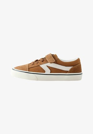 Bruine lage sneaker met witte zigzagstreep, veters aan de voorkant, klittenbandsluiting en witte rubberen zool met zwarte rand.