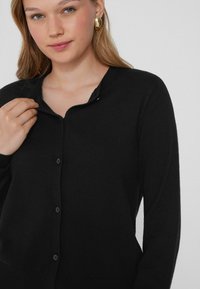 Schwarze Knopfleiste-Cardigan aus weichem Material, mit V-Ausschnitt, langen Ärmeln und einer dezenten Rippstruktur am Saum.