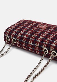 Small rectangular handbag with burgundy, navy, and beige tweed fabric, silver chain straps, and a triangular Guess logo plaque.