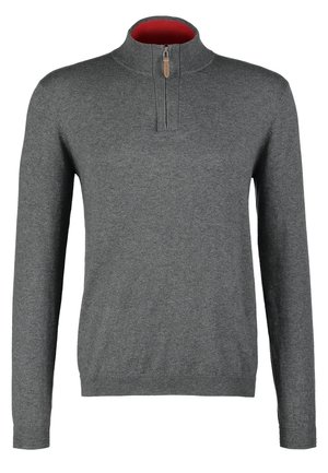 Homme marchant portant un pull gris à fermeture éclair au quart, pantalon noir, baskets blanches et portant un sac à bandoulière noir.