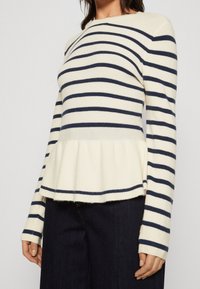 Pull en rayures crème et marine, avec un ourlet peplum, des manches longues avec des poignets rayés et une texture côtelée. Design décontracté.