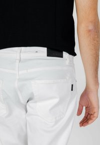 Vaqueros de denim blanco con una etiqueta de cuero en la cintura y en los bolsillos traseros. La textura parece suave. Costuras visibles que acentúan las costuras.