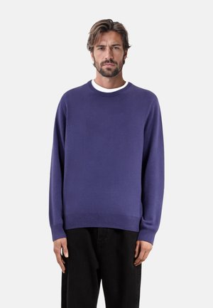 Suéter de punto morado con un cuello redondeado y puños acanalados, hecho de material suave. Combinado con pantalones de pana negros.