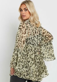 Plisserad blus i genomskinligt, lätt tyg med ett blommönster i grönt, crème och guld. Långa, trumpetformade ärmar och rund halsringning.