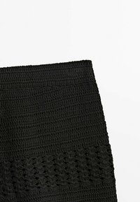 Produit au crochet noir, présentant des motifs texturés et un design côtelé. Le matériau semble doux et flexible, adapté à diverses utilisations.