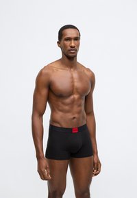 Melni bokseršorti ar sarkanu logotipa jostas vietu, izgatavoti no mīksta, elastīga auduma. Raksturīgs pieguļošs dizains un gluda tekstūra.