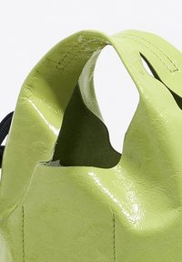 Zielona torba z ekoskóry o teksturowym wykończeniu. Posiada uchwyty w kształcie wycięcia oraz detale w postaci szwów. Kompaktowy design z gładkim, błyszczącym wyglądem.