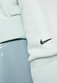 Mintgroene sweatshirt met textuurstof, met een zwart Nike-logo op de mouw, gecombineerd met lichtblauwe leggings met ribbelaccenten.