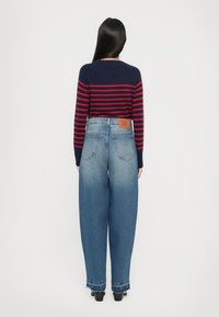 Maglione a righe blu navy e rosse con scollatura rotonda, abbinato a jeans di denim blu chiaro a gamba larga con orlo sfrangiato e applicazione in pelle.