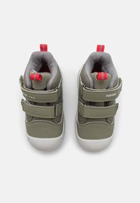 Zielone wodoodporne buty z dwoma rzepami, z szarym wykończeniem i czerwonymi pętlami. Okrągła biała gumowa podeszwa z teksturowanym gripem.