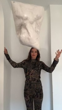 Γυναίκα που φοράει ρούχα με λεοπάρ σχέδιο πετάει ένα μεγάλο διαφανές μαξιλάρι γεμάτο με λευκό υλικό, μπροστά σε απλό λευκό φόντο.