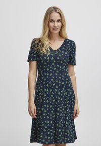 Námořnické šaty s krátkými rukávy, véčkovým výstřihem a zeleným květinovým potiskem. Měkká tkanina v rozšířeném střihu, dosahující k polovinu lýtek s volnějším střihem.