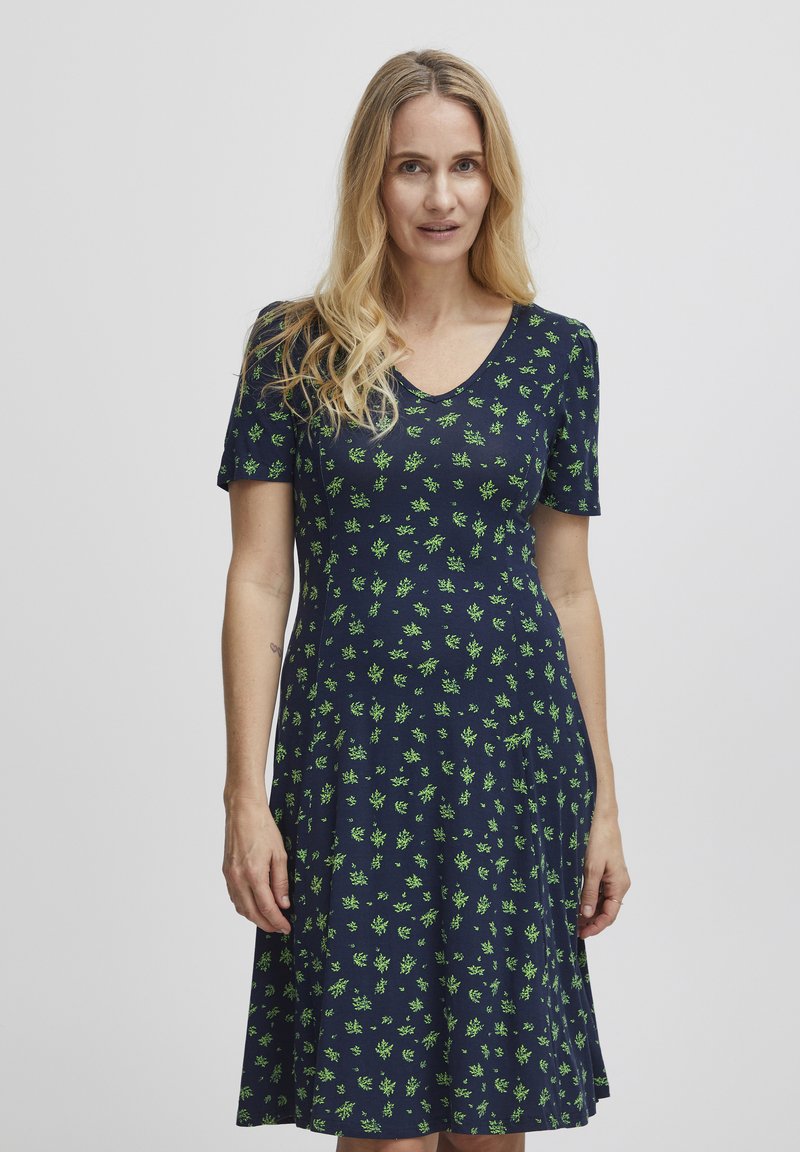 Námořnické šaty s krátkými rukávy, véčkovým výstřihem a zeleným květinovým potiskem. Měkká tkanina v rozšířeném střihu, dosahující k polovinu lýtek s volnějším střihem.