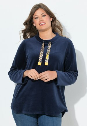 Pull en polaire doux de couleur bleu marine, avec un col haut et des manches longues. Il est doté de deux cordons de tirage imprimés léopard avec des embouts jaunes.