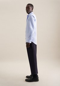 Lichtblauwe button-up shirt met lange mouwen, gecombineerd met donkere broeken en zwarte schoenen, gepresenteerd tegen een neutrale achtergrond.