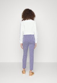 Bílá bavlněná košile s dlouhými rukávy, spárovaná s texturovanými fialovými kalhotami a béžovými platformovými sandály. Jednoduchý design a přiléhavý střih.