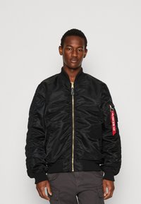 Casaco bomber preto com acabamento satin, punhos e barra em malha canelada. Zíper dourado, bolso lateral com detalhe de etiqueta vermelha e design de mangas franzidas.